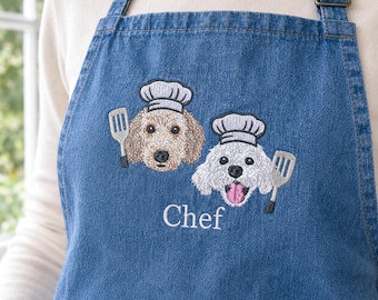 Könnte beinhalten: Eine blaue Jeansschürze mit einer Stickerei von zwei Hunden, die weiße Kochmützen tragen. Jeder Hund ist neben einem Pfannenwender abgebildet. Das Wort Chef ist in weißem Garn unter den Hunden eingestickt. Die Schürze hat verstellbare Träger.