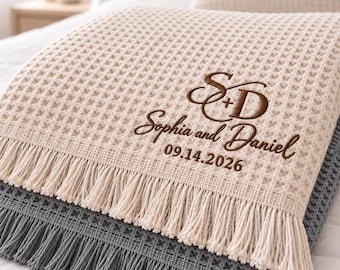 Könnte beinhalten: Eine beige Waffelstrickdecke mit Fransenbesatz, bestickt mit braunem Text, der S+D, Sophia and Daniel und das Datum 09.14.2026 zeigt. Die Decke liegt über einer dunkelgrauen Waffelstrickdecke mit passendem Fransenbesatz.