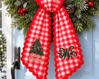 Könnte beinhalten: Eine rot-weiß karierte Stoffschleife mit gewelltem Rand. Der linke Teil zeigt einen gestickten grünen Weihnachtsbaum mit dem Text Merry Christmas, während der rechte Teil einen großen, dekorativen, grün gestickten Buchstaben W aufweist.