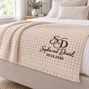 Parchment waffle throw featuring a personalized wedding embroidery positioned near the lower corner.
The design includes a large intertwined “S + D” monogram, “Sophia and Daniel” in script, and the date “09.14.2026” below.
All details are embroidered in deep brown thread for a clear contrast against the light Parchment fabric.
The elegant corner placement creates a personalized monogrammed wedding throw design.