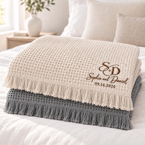 Parchment and Gusty Grey waffle throws featuring a personalized wedding monogram embroidered near the lower corner.
The Parchment throw displays an elegant “S + D” monogram with “Sophia and Daniel” and the date “09.14.2026” stitched below.
Rich brown thread creates the initials, script names, and date with a clean raised embroidery finish.
The corner placement keeps the personalized design visible while highlighting the textured waffle fabric and fringe.