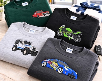 Könnte beinhalten: Eine Kollektion von vier Gildan Rundhals-Sweatshirts mit gestickten Fahrzeugmotiven. Das dunkelgrüne Sweatshirt zeigt einen roten LKW, das schwarze ein grünes Motorrad, das hellgraue einen weißen SUV und das dunkelgraue einen blauen Sportwagen.