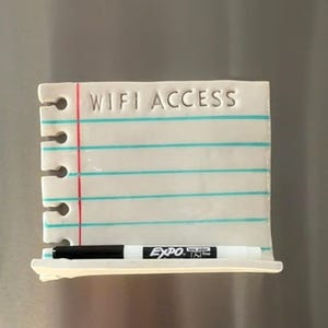 May include: A rectangular white ceramic magnetic board shaped like a piece of notebook paper with a red vertical margin line and horizontal blue lines. The text WIFI ACCESS is embossed at the top. A black Expo dry erase marker rests on the ledge.
