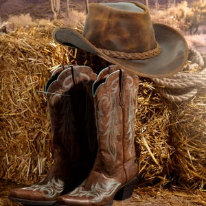 May include: A brown leather cowboy hat with a braided band and a pair of brown leather cowboy boots featuring light blue decorative stitching on the shaft and toe. The boots have a tall silhouette and a stacked heel, while the hat has a wide brim.