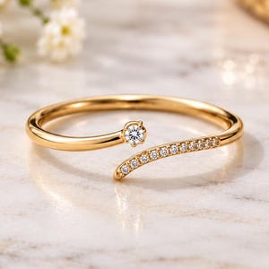 Könnte beinhalten: Ein offener Ring aus poliertem Gelbgold mit einem einzelnen runden Brillantschliff-Diamanten an einem Ende und einer Reihe kleiner Pavé-gefasster Diamanten entlang des anderen spitz zulaufenden Endes für ein zartes Erscheinungsbild.