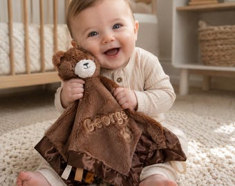 Peut inclure: Une couverture de sécurité en peluche marron avec une tête d'ours en peluche et un museau crème. Le tissu doux est brodé du nom George et d'une empreinte de patte, avec une bordure en satin marron foncé et des petites étiquettes en ruban.