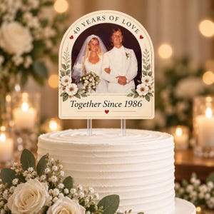 May include: An arched cake topper featuring a vintage wedding photograph of a couple, with the text 40 YEARS OF LOVE and Together Since 1986. The design includes floral illustrations on the sides and two clear acrylic stakes for insertion.