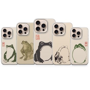 May include: Five smartphone cases featuring various artistic frog illustrations in green, black, and beige tones. Each case displays a unique frog character, some with red Japanese text stamps. The designs include a frog eating, sitting on a toilet, and stylized outlines, all set against a neutral background.