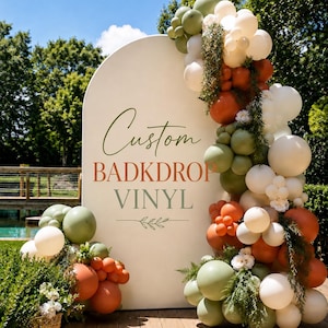 Könnte beinhalten: Ein großes bogenförmiges Hintergrundschild mit dem Text Custom BADKDROP VINYL in grüner und orangefarbener Schrift. Das Schild ist mit einem Balloncluster in Salbeigrün, gebranntem Orange und Creme sowie grünem Blattwerk verziert.