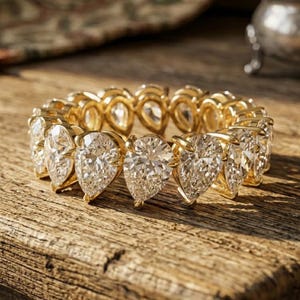 Könnte beinhalten: Ein goldener Eternity-Ring mit einer durchgehenden Reihe von klaren, birnenförmig geschliffenen Edelsteinen. Der Ring besteht aus einer Gelbgoldfassung, die jeden tropfenförmigen Stein mit Krappen hält und ein kreisförmiges Design bildet.