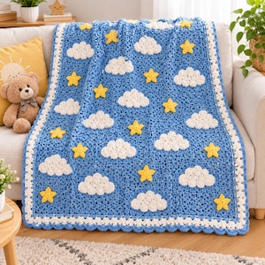 May include: A blue crochet blanket featuring a repeating pattern of white clouds and yellow stars. The blanket has a white scalloped border and a textured knit construction, displaying a celestial theme across the entire rectangular surface.
