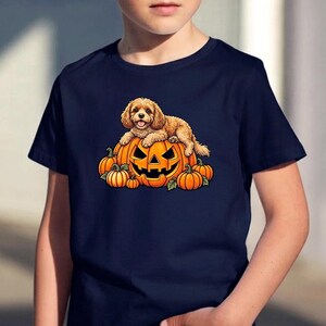 Puede incluir: Una camiseta azul marino de manga corta con un estampado gráfico de un perro de pelo rizado color marrón claro descansando sobre una gran calabaza de Halloween naranja, rodeado de varias calabazas naranjas más pequeñas con hojas verdes.