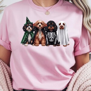 Peut inclure: Un t-shirt rose clair à manches courtes orné d'un motif représentant quatre chiens déguisés pour Halloween. Les chiens portent un chapeau et une cape de sorcière verts, une cape de vampire noire, un costume de squelette noir et un drap de fantôme.