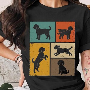 May include: A black t-shirt featuring a graphic print of five dog silhouettes in various poses. The design is divided into rectangular panels with distressed textures in muted shades of teal, orange, yellow, cream, and brown on the front.