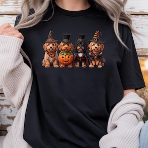 May include: A black t-shirt featuring a graphic print of four dogs dressed in Halloween costumes. The dogs are wearing hats, a pumpkin suit, a vampire cape, and a striped dress. The design includes orange, black, and brown colors.