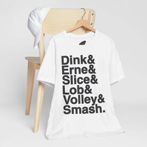 May include: White t-shirt with black text that reads "Dink & Erne & Slice & Lob & Volley & Smash."