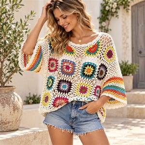 May include: A cream-colored crochet top featuring a vibrant granny square pattern in various colors including red, yellow, blue, and purple, with wide sleeves and a scalloped neckline, paired with light blue denim shorts with a frayed hem.