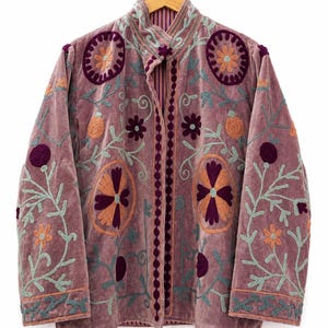 May include: A mauve velvet jacket featuring a mandarin collar and long sleeves. The garment is decorated with intricate floral embroidery in shades of dark purple, light blue, and orange, with a vertical row of dark purple circular accents.
