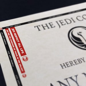 May include: A white certificate with black text that reads "The Jedi Council" and a black symbol with a white background. The text "Jedi Respect All Life" is printed in red on the side of the certificate.