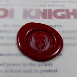 May include: A red wax seal with a white Jedi symbol. The seal is on a white document with the text "JEDI KNIGHT" printed in red.