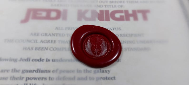 May include: A red wax seal with a white Jedi symbol. The seal is on a white document with the text "JEDI KNIGHT" printed in red.