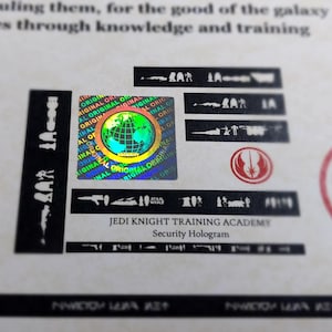 May include: A holographic sticker with a globe design and the text "ORIGINAL" repeated around the globe. The sticker also has the text "JEDI KNIGHT TRAINING ACADEMY" and "Security Hologram" below it.