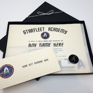 May include: A black box with a white Starfleet Academy diploma inside. The diploma has a blue and silver Starfleet logo and the text "STARFLEET ACADEMY" and "THE FACULTY OF STARFLEET ACADEMY HEREBY ACKNOWLEDGE THAT ANY NAME HERE HAS FULFILLED ALL REQUIREMENTS FOR STARFLEET GRADUATE INSTRUCTION AND IS ENTITLED TO THIS DEGREE".