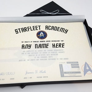 May include: A Starfleet Academy diploma in a black presentation box. The diploma is printed on parchment paper and features the Starfleet Academy logo and the text "STARFLEET ACADEMY". The diploma is signed by "James T. Kirk" and "Hikaru Sulu".