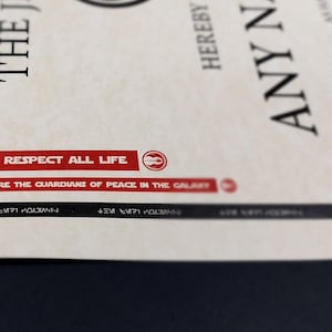 May include: A close-up of a certificate with the text "JEDI RESPECT ALL LIFE" and "JEDI ARE THE GUARDIANS OF PEACE IN THE GALAXY" printed in red on a white background. The certificate also includes the text "THE JEDI" and "HEREBY ANY NAME THE RELEVANT TASKS AND EARNED JEDI ALL PR"