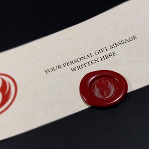 May include: A white card with a red Star Wars Rebel Alliance symbol and the text "YOUR PERSONAL GIFT MESSAGE WRITTEN HERE". A red wax seal with the Rebel Alliance symbol is on the card.