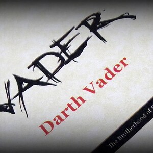 May include: A black and white illustration of the word "Vader" with a red and white text overlay that reads "Darth Vader" and "The Brotherhood of Darkness" in the bottom right corner.