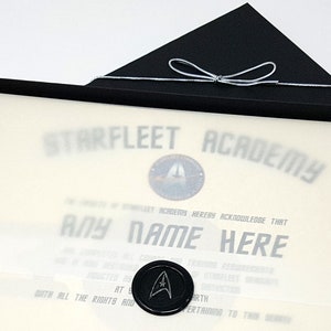 May include: A black box with a white certificate inside. The certificate is for Starfleet Academy and says "THEREBY ACKNOWLEDGE THAT ANY NAME HERE".