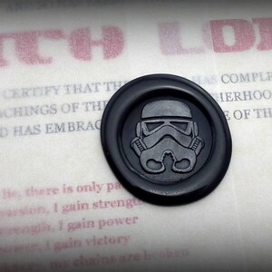 May include: A black wax seal with a white Star Wars Stormtrooper helmet design. The seal is on a white background with the text "SITH LORD" in red letters above it. The text below the seal reads "THIS IS TO CERTIFY THAT THE... HAS COMPLETED TRAINING IN THE... HERHOOD OF DARKNESS... OF THE FORCE."