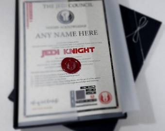 May include: A red wax seal with a Jedi symbol on a certificate that reads "The Jedi Council" and "Jedi Knight". The certificate is in a black box with a black envelope.
