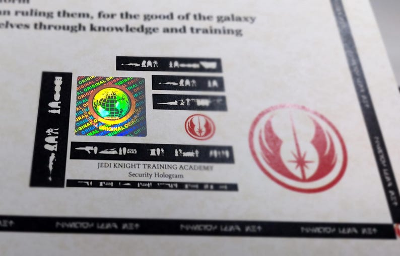 May include: A close-up of a holographic sticker with the text "JEDI KNIGHT TRAINING ACADEMY" and the words "Security Hologram". The sticker features a colorful globe with the words "ORIGINAL" repeated around it. The sticker is on a white background with a red and white Jedi symbol.