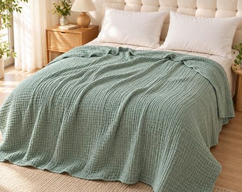 May include: A sage green textured cotton blanket draped over a bed with a tufted headboard and two white pillows. The blanket features a distinct crinkled, multi-layered grid pattern across its entire surface, providing a soft and layered appearance.