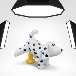 Puede incluir: Una figura de perro de cerámica blanca con manchas negras, representada en posición de pie con una pata levantada. Un pequeño objeto cilíndrico de color amarillo está colocado debajo de la pata levantada. La figura tiene un acabado liso.