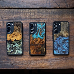 May include: Three black phone cases with unique wooden burl designs. The cases feature a camera cutout and a black frame. The wood grain patterns include shades of brown, green, and blue, creating a natural and artistic look.