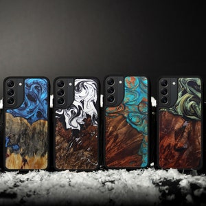May include: Four black phone cases with unique wood and resin designs. The cases feature a variety of colors, including blue, white, turquoise, and green, set against a natural wood grain. The cases are displayed on a snowy surface.