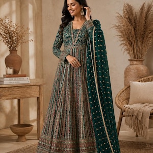 Puede incluir: Un vestido Anarkali largo hasta el suelo de color verde esmeralda con mangas largas, escote en V y bordados intrincados en dorado y multicolor por todo el cuerpo y la falda. Una dupatta verde transparente a juego con lunares dorados.