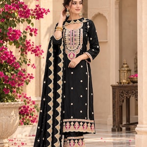 Könnte beinhalten: Ein dreiteiliges schwarzes Set bestehend aus einer langärmeligen Tunika mit aufwendiger goldener und magentafarbener Stickerei am Ausschnitt und Saum, einer passenden weiten Hose und einem schwarzen Dupatta mit goldener Bogenkante.