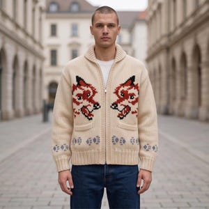 May include: A cream-colored knit zip-up cardigan featuring a repeating fox head pattern in red, black, and white across the chest. The garment includes a ribbed collar, two front pockets, and a row of small blue paw print motifs along the hem.