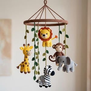 May include: A hanging nursery mobile featuring five crocheted animal figures: a yellow lion, a yellow giraffe with brown spots, a brown monkey, a gray elephant, and a black and white zebra, suspended from a brown circular frame with green vines.