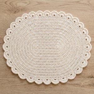 Può includere: Un centrino all'uncinetto di colore bianco sporco, di forma ovale, caratterizzato da un motivo centrale denso e testurizzato e da un bordo smerlato decorativo. L'oggetto è realizzato con un punto uniforme su tutta la superficie.