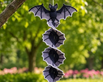 May include: A hanging crochet decoration featuring a dark gray bat at the top with outstretched wings, connected to a spiraling, vertical series of three additional bat-wing segments in alternating shades of dark gray and light gray yarn.