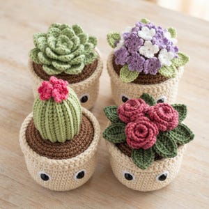 May include: Four crocheted plants in cream-colored pots with black safety eyes. The plants include a green succulent, a purple and white flower cluster, a ribbed green cactus with a pink top, and a cluster of dark pink roses with green leaves.