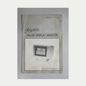 May include: A white instruction manual for a Phoenix Color Display Monitor, Model PX-II, III, IV. The cover features the brand name in a stylized script, the product name in bold text, and a black and white photograph of the monitor unit.