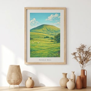 May include: A framed wall art print featuring a landscape illustration of Pendle Hill with rolling green fields, a bright blue sky with white clouds, and the text PENDLE HILL printed in black at the bottom center of the white border.