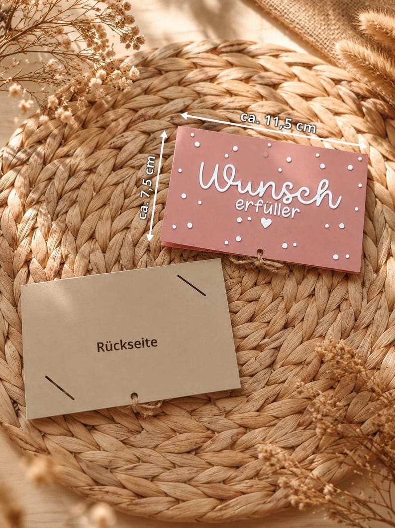 Peut inclure: Une carte rectangulaire rose poudr&eacute; avec le texte blanc "Wunsch erf&uuml;ller", un petit c&oelig;ur et des points blancs. Elle mesure 11,5 cm sur 7,5 cm. En dessous se trouve une carte beige clair marqu&eacute;e "R&uuml;ckseite" avec des fentes aux coins.