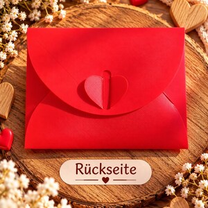 May include: A bright red envelope featuring a heart-shaped closure tab on the front flap. Below the envelope, a small white rectangular label displays the text "R&uuml;ckseite" with a small heart icon centered between two horizontal lines.